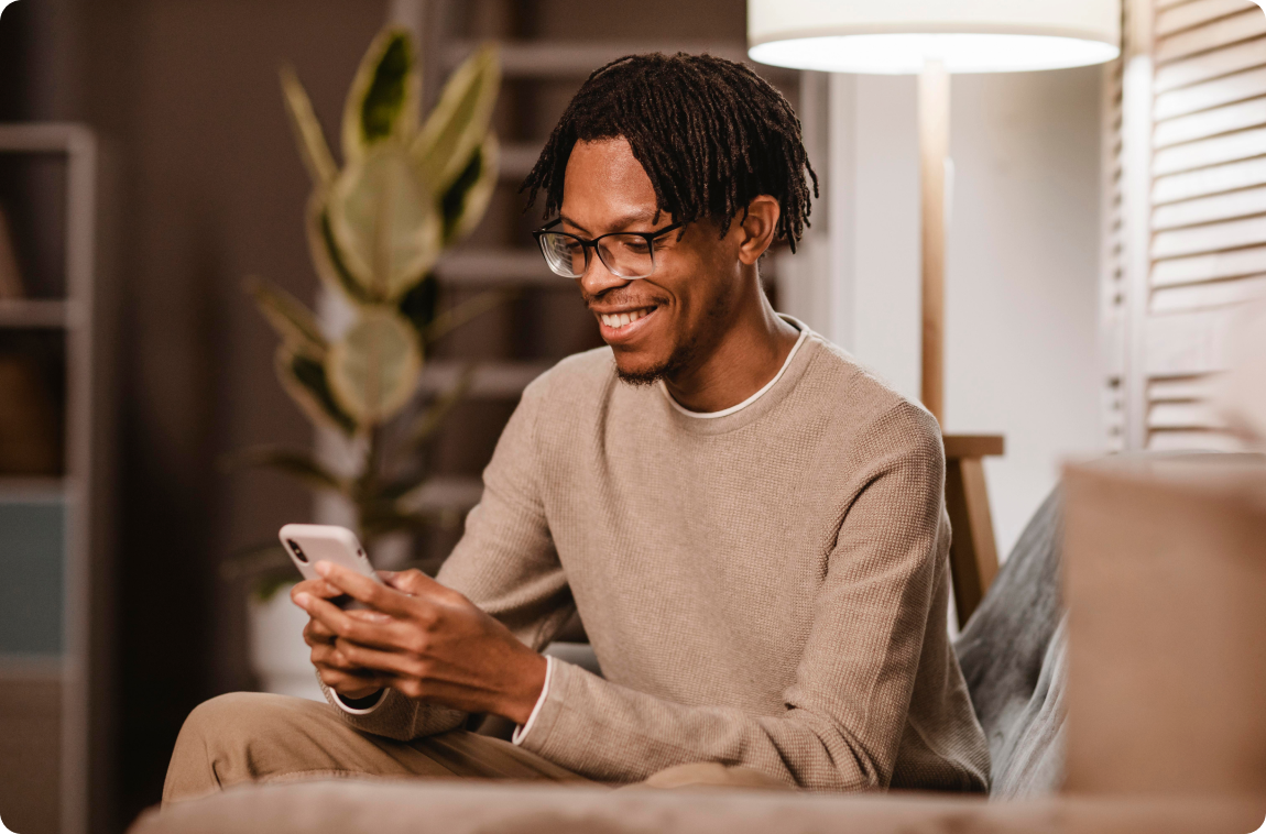 homem negro com moleton bege mexendo no celular e sorrindo